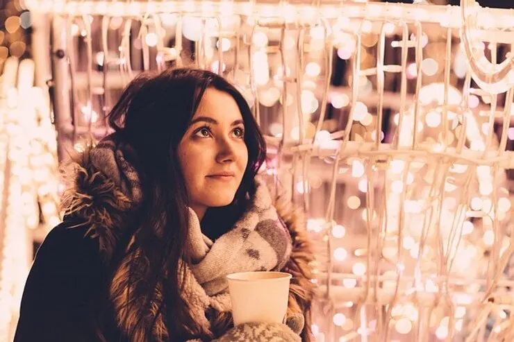 A woman holding a warm drink in front of a wall of holiday lights