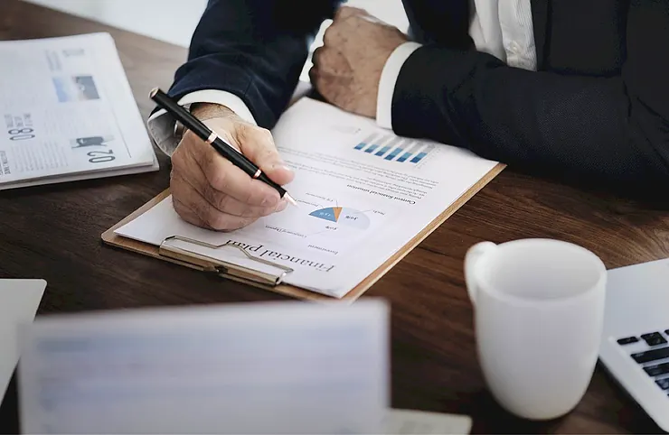 A person reviewing revenue charts on paper next to a laptop and coffee