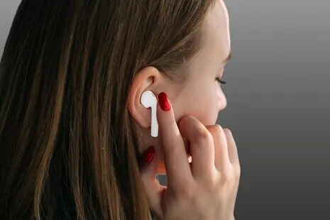 A woman using wireless earbuds to speak to a voice assistant